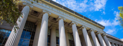 Building 7 in Killian Court, a building with columns, sits between trees on a sunny day.