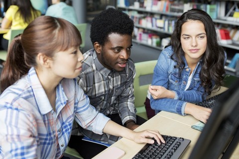 Three people gather around a laptop.