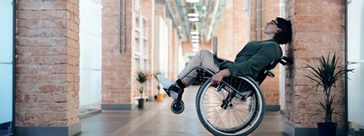 a person using a wheelchair, leaning against a wall and propping the wheelchair on two wheels