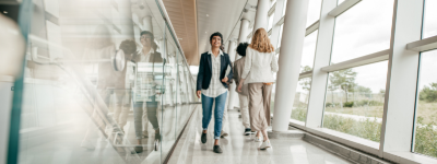 a person wearing business casual, walking down a hallway, past another person who is walking in the opposite direction