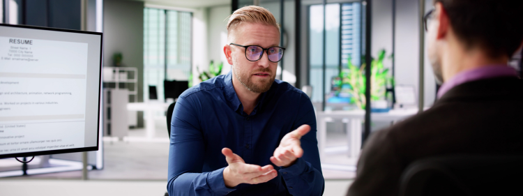 a man wearing a blue shirt and glasses, answering a question during an interview
