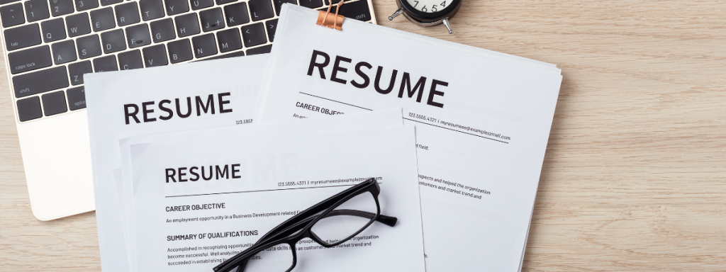 a few resumes lie on top of a computer with a pair of glasses