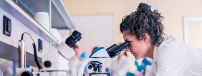 A woman looks into a microscope in a lab.
