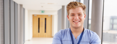 A man wearing scrubs smiles at the camera.