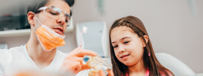 A man in a mask shows a young patient a clear mold of teeth.