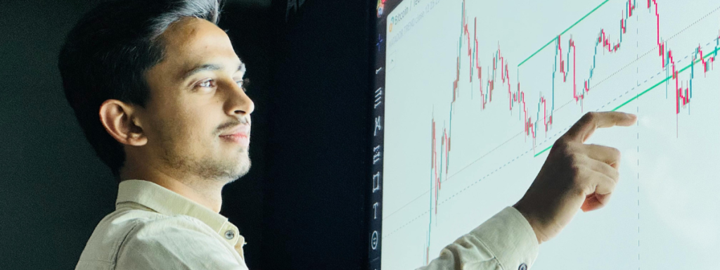 a man standing in front a graph depicting data, pointing at something on it 