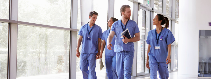 four people wearing medical scrubs walk in a bright hallway