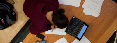Student bent over papers and laptop