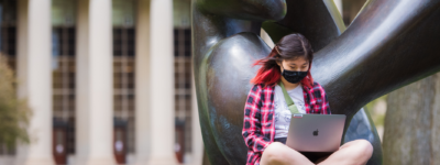 A person sits in front of a statue holding a laptop.
