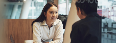 A person leans forward, smiling, as she listens to another person.