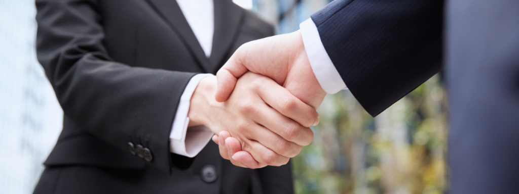 two people shaking hands while wearing suits