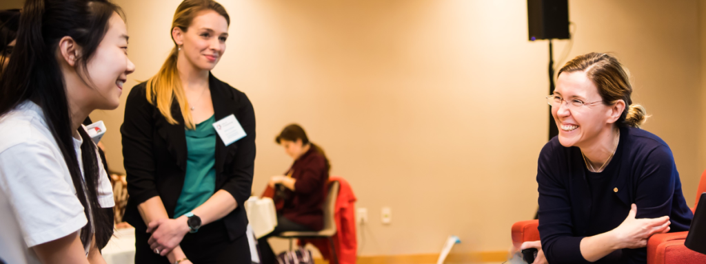 A professor chats with graduate students, smiling, at an event.