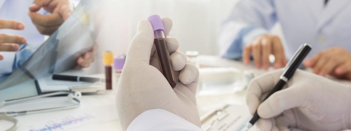 A gloved hand holding a vial while another hand writes notes on a sheet.