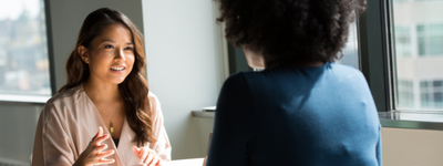Two professionally-dressed women talk in a bright space.